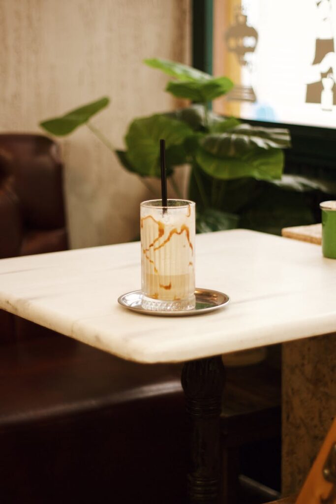 A caramel iced coffee served in a glass with a straw on a marble table in a cozy cafe.