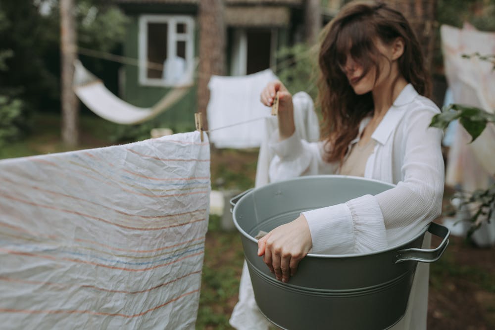 Young woman hanging laundry outdoors with a clothesline in a rustic setting.