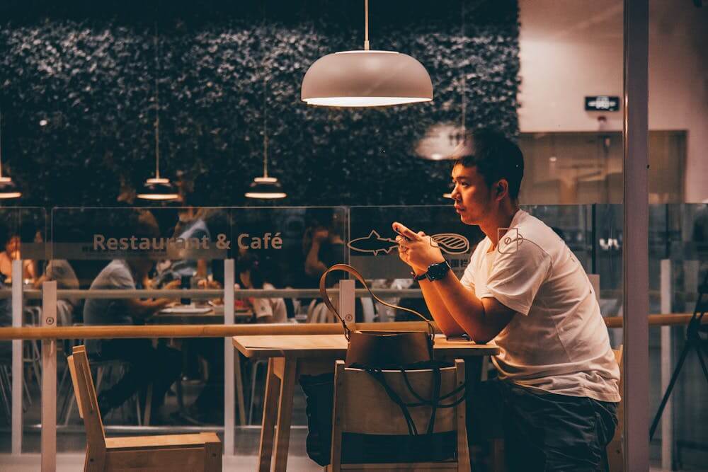 Man sitting alone in a cafe, pensive and using his phone, under warm lighting.